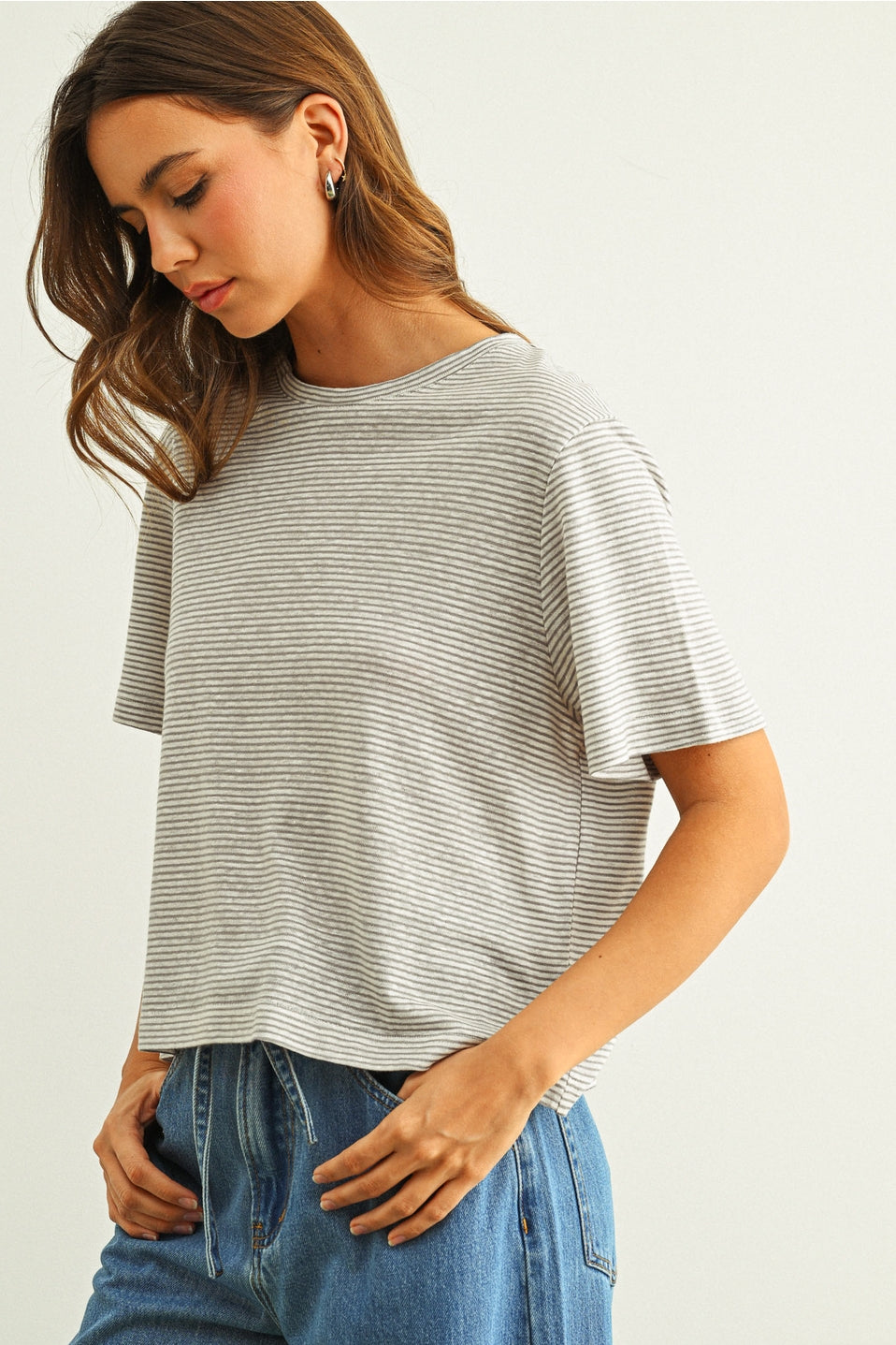 Woman looking down wearing a grey & white striped t-shirt and jeans on a white background