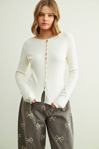 Woman wearing a cream sweater and gray pants with bow patterns on a light background