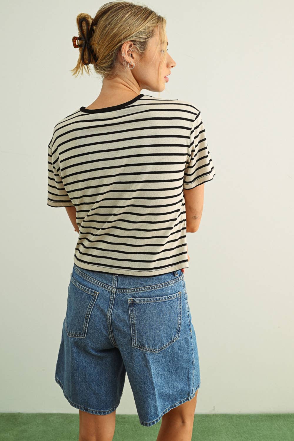 Person wearing a black and white striped shirt and denim shorts against a plain background