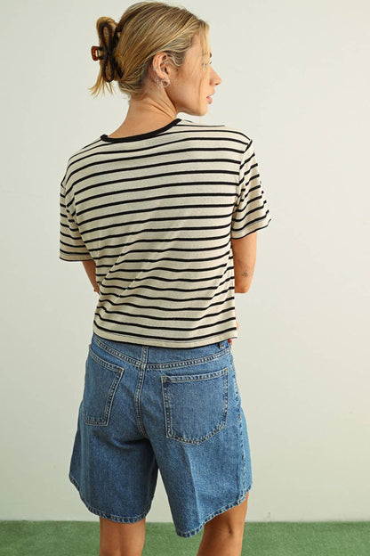 Person wearing a black and white striped shirt and denim shorts against a plain background