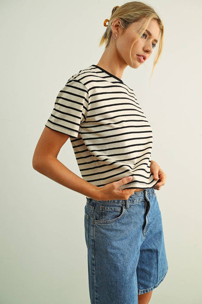 Woman wearing a black and white striped shirt and denim shorts against a plain background