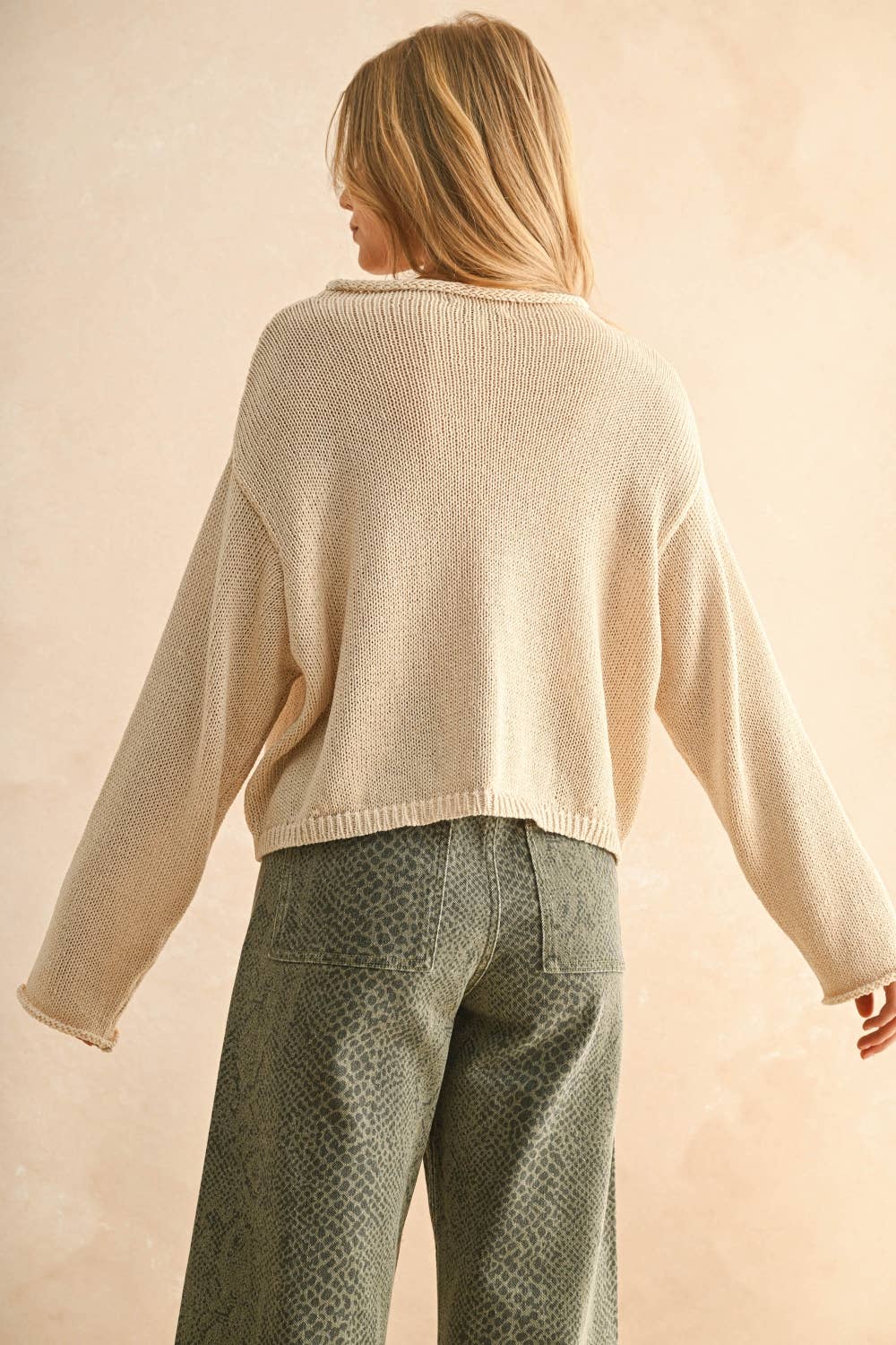 Back view of woman wearing a cream sweater and patterned pants against a beige background