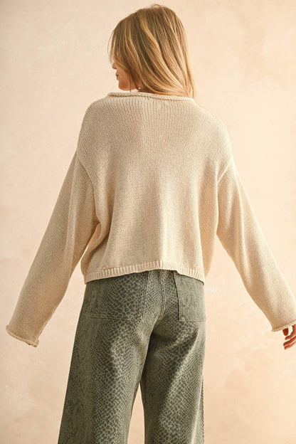 Back view of woman wearing a cream sweater and patterned pants against a beige background