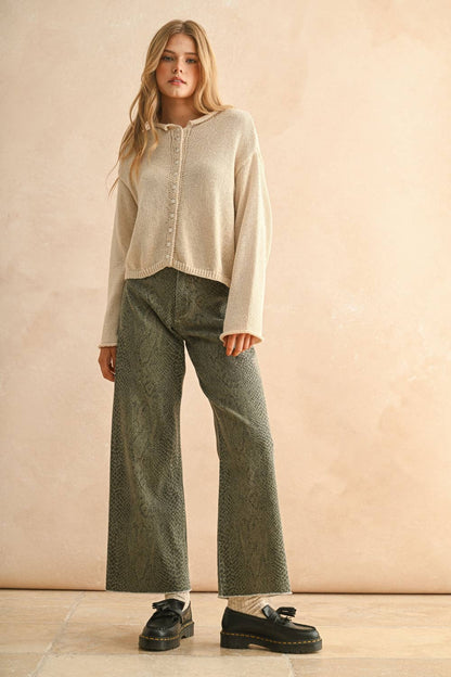 Woman wearing a cream cardigan and green pants against a beige background