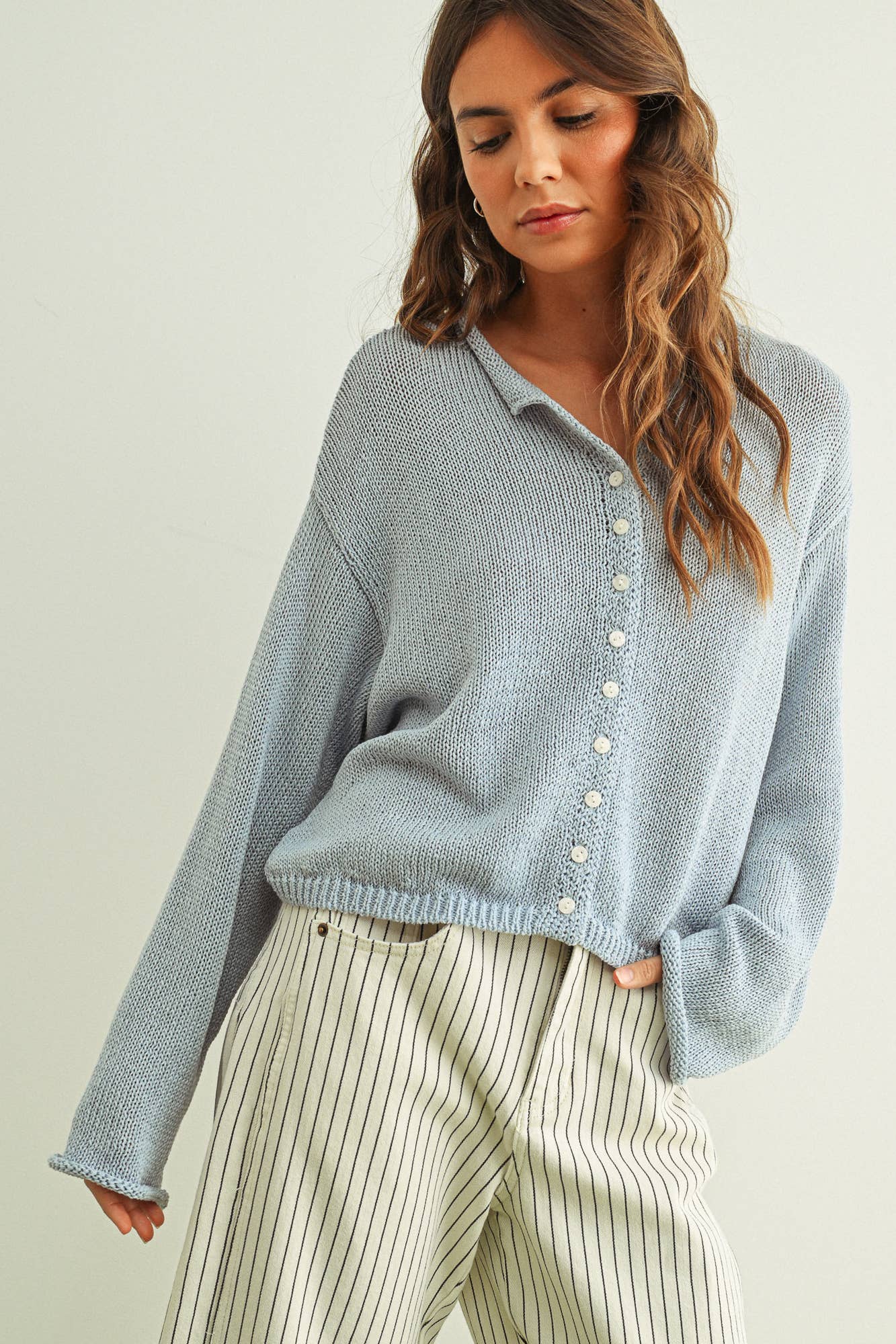 Woman wearing a sky blue knitted cardigan and striped pants against a plain background