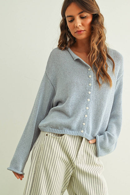Woman wearing a sky blue knitted cardigan and striped pants against a plain background