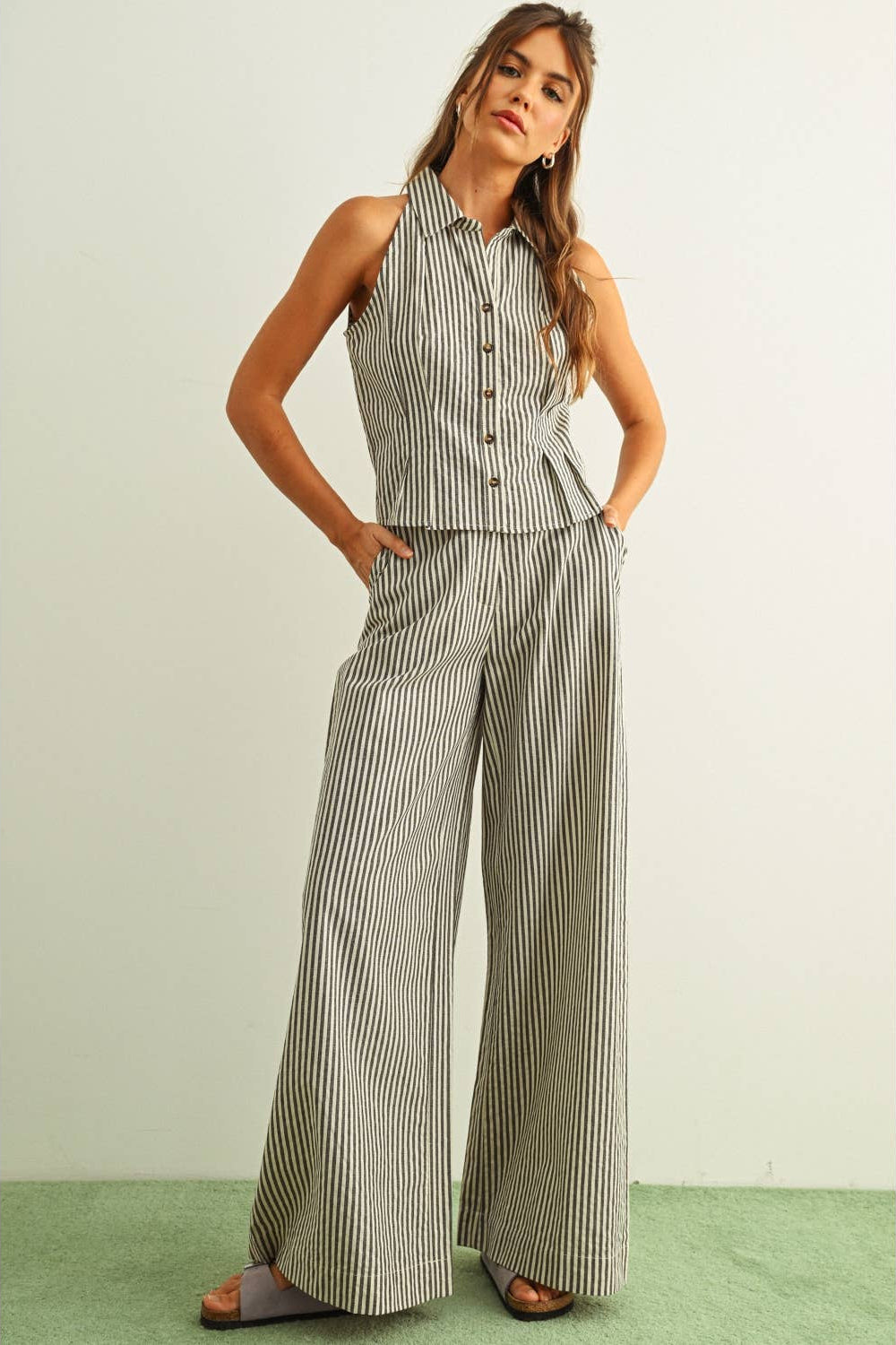 Woman wearing a striped sleeveless top and black striped wide-leg pants on a light green background