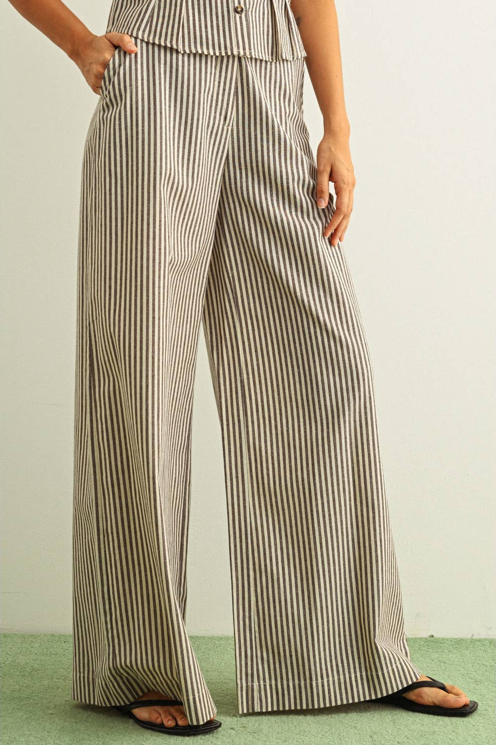 Person wearing a pair of wide-leg striped brown and beige pants on a plain background
