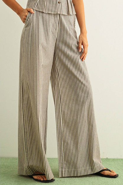 Person wearing a pair of wide-leg striped brown and beige pants on a plain background