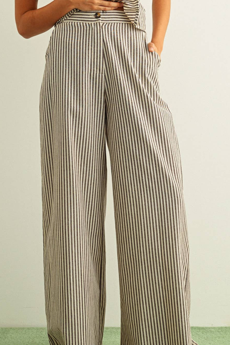 A person wearing high-waisted, wide-leg trousers with vertical beige and dark brown stripes, shown from the waist down against a plain light background.