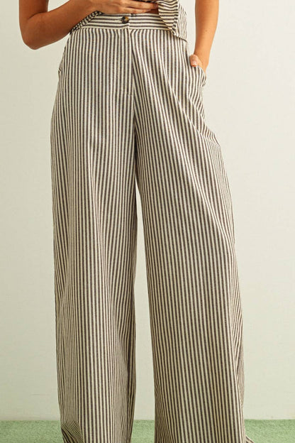 A person wearing high-waisted, wide-leg trousers with vertical beige and dark brown stripes, shown from the waist down against a plain light background.
