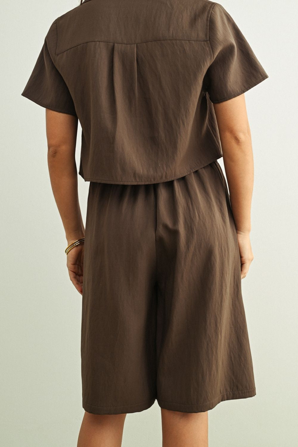 A person shown from the back wearing a matching brown short-sleeve top and shorts set against a plain light gray background.