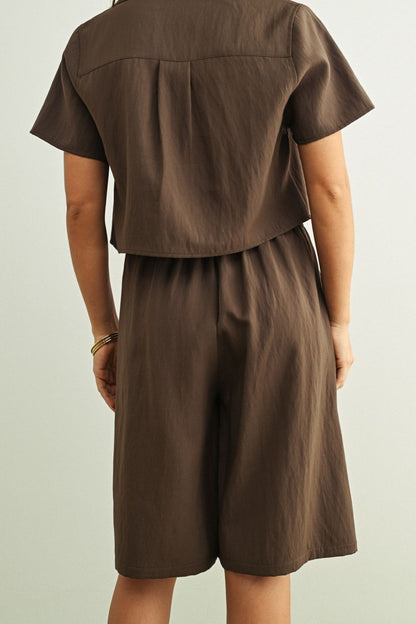 A person shown from the back wearing a matching brown short-sleeve top and shorts set against a plain light gray background.