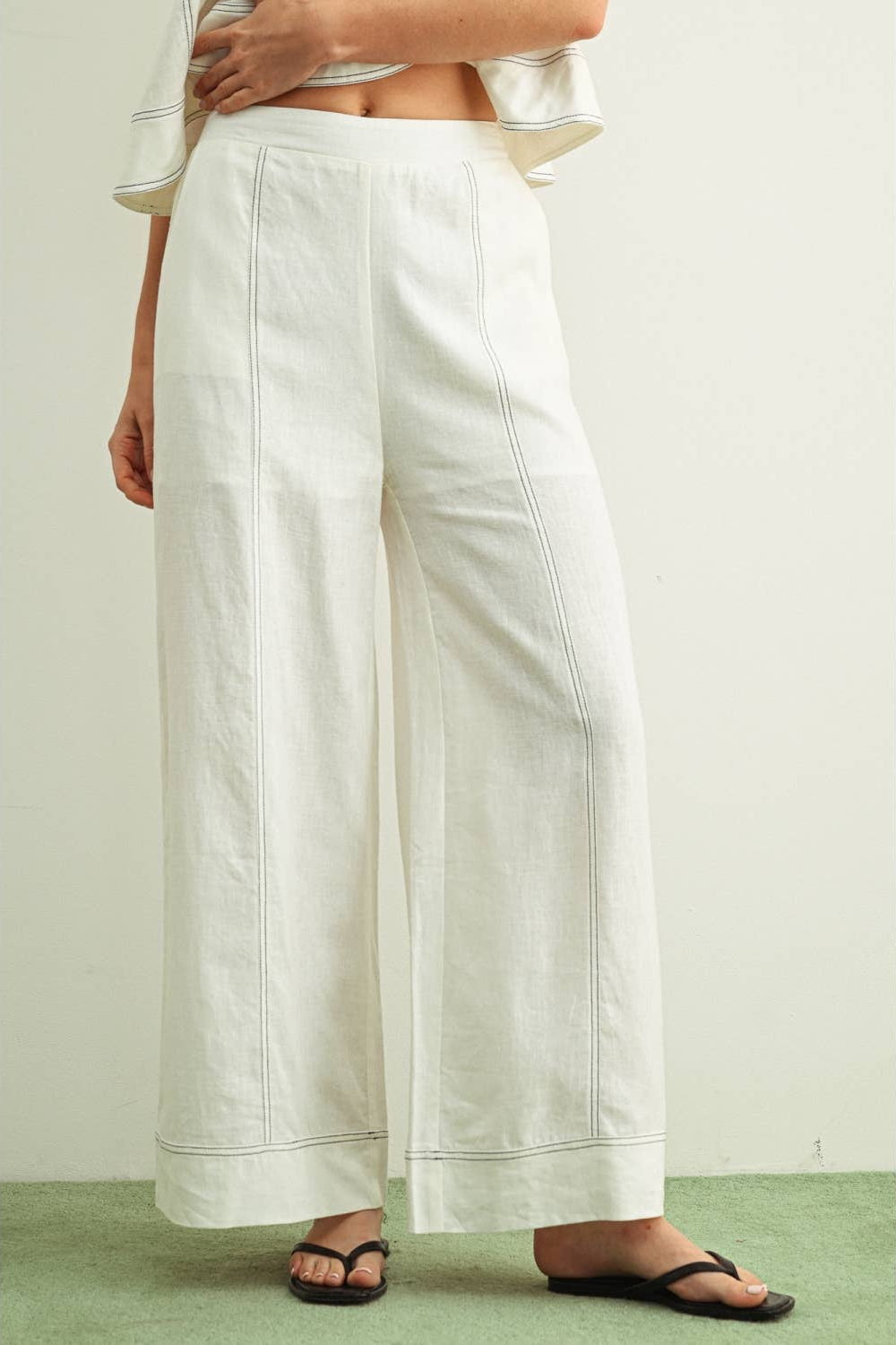 Person wearing stitched white wide-leg linen pants on a plain background