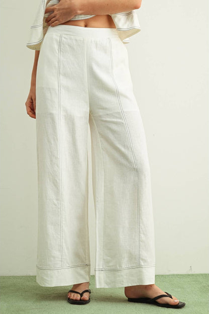 Person wearing stitched white wide-leg linen pants on a plain background
