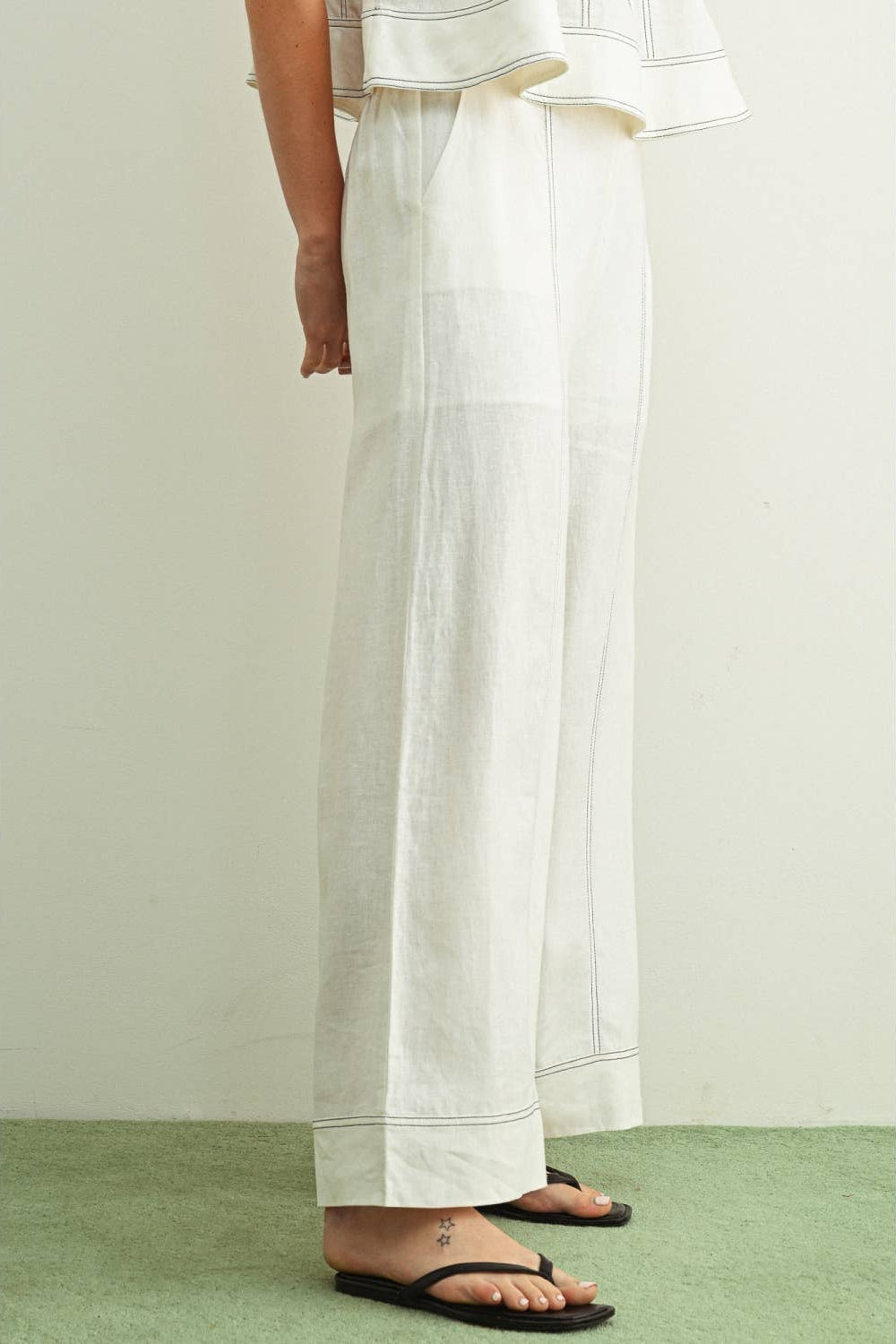 Side view of person wearing white linen pants on a plain background