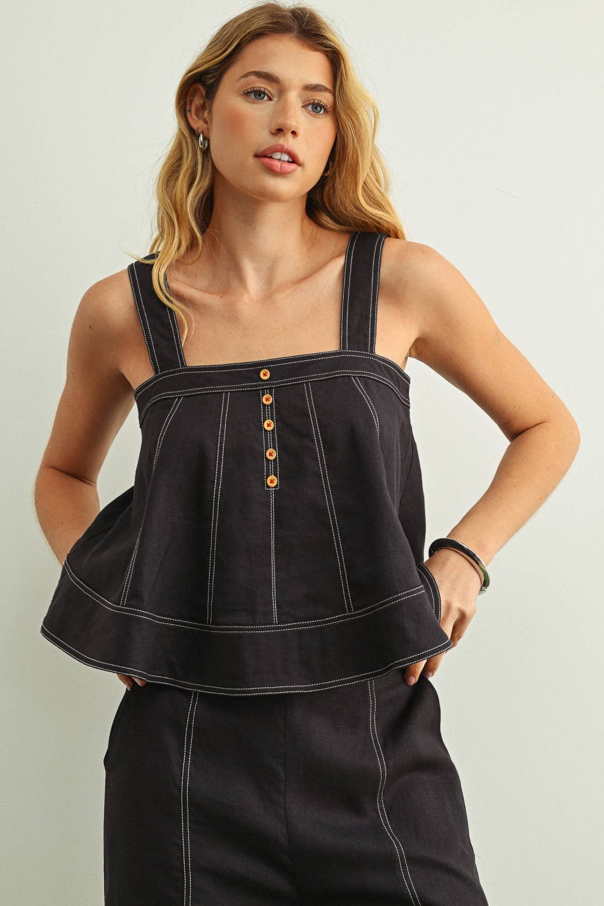 Woman wearing a Navy stitched peplum top with gold buttons against a light background