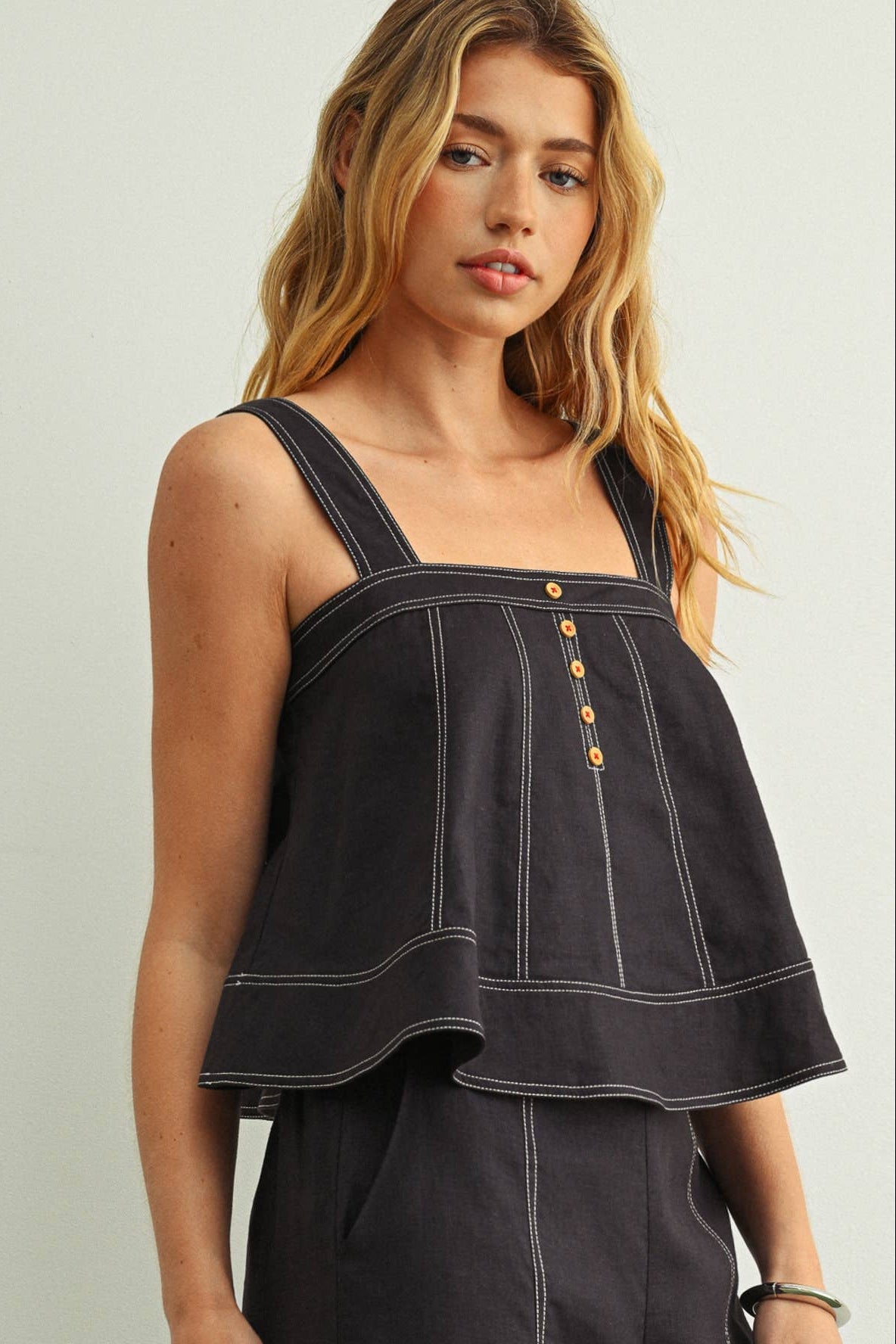 Woman wearing a navy sleeveless top with button details against a plain background