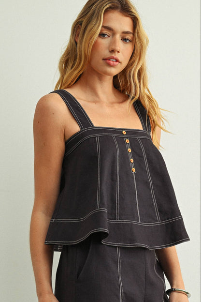 Woman wearing a navy sleeveless top with button details against a plain background