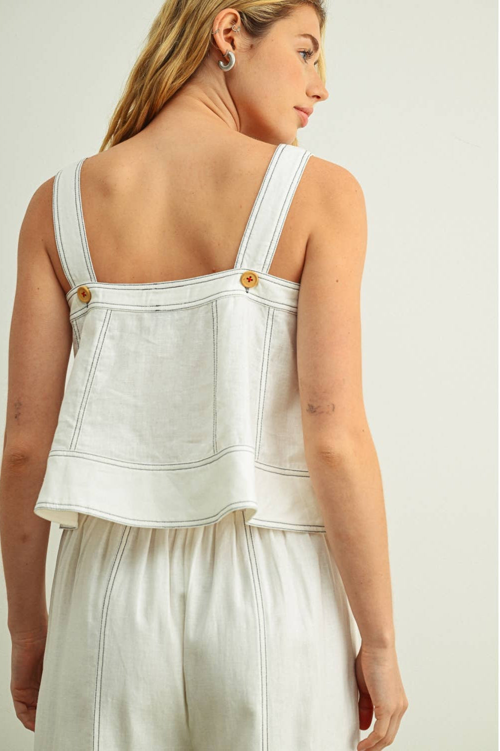 Woman wearing a white top with stitching on a plain background