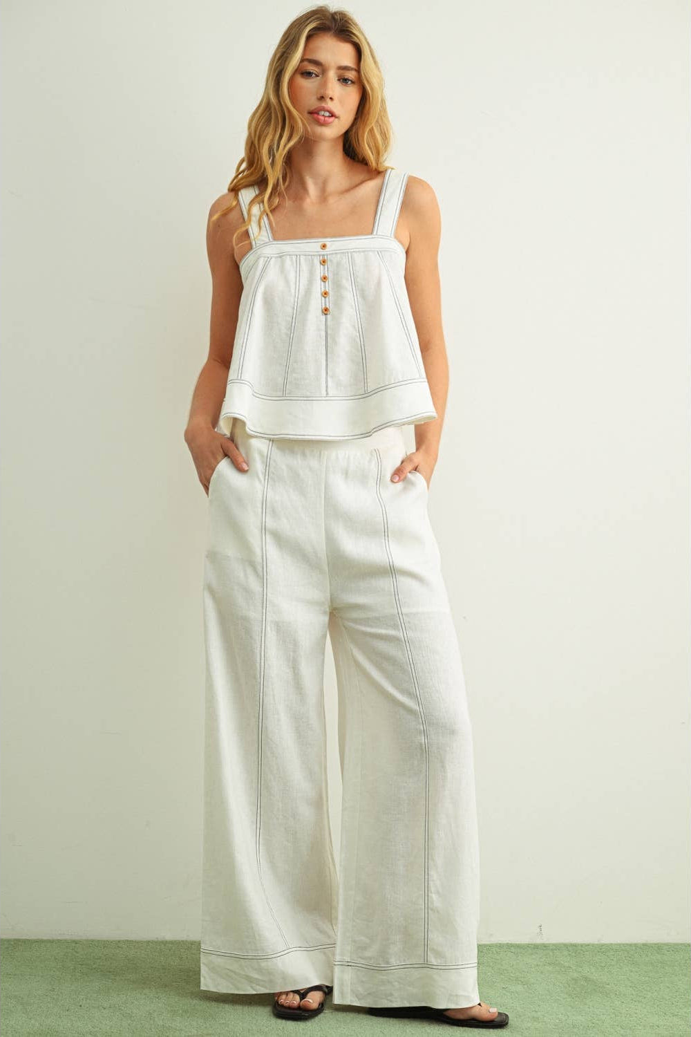 Woman wearing a white stitched top and wide-leg pants against a plain background