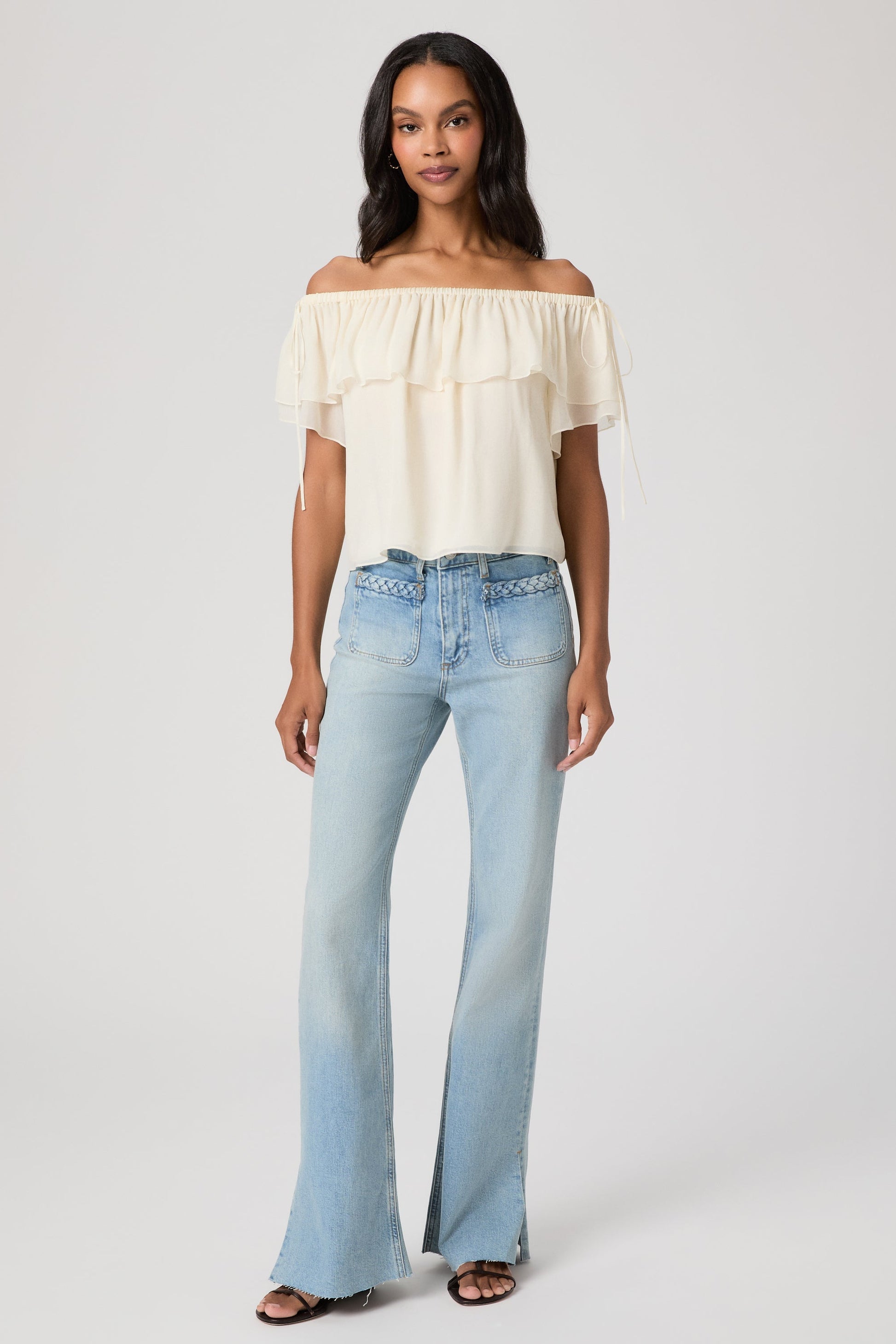 Woman wearing a white off-shoulder top and light blue montebello sofia jeans on a white background