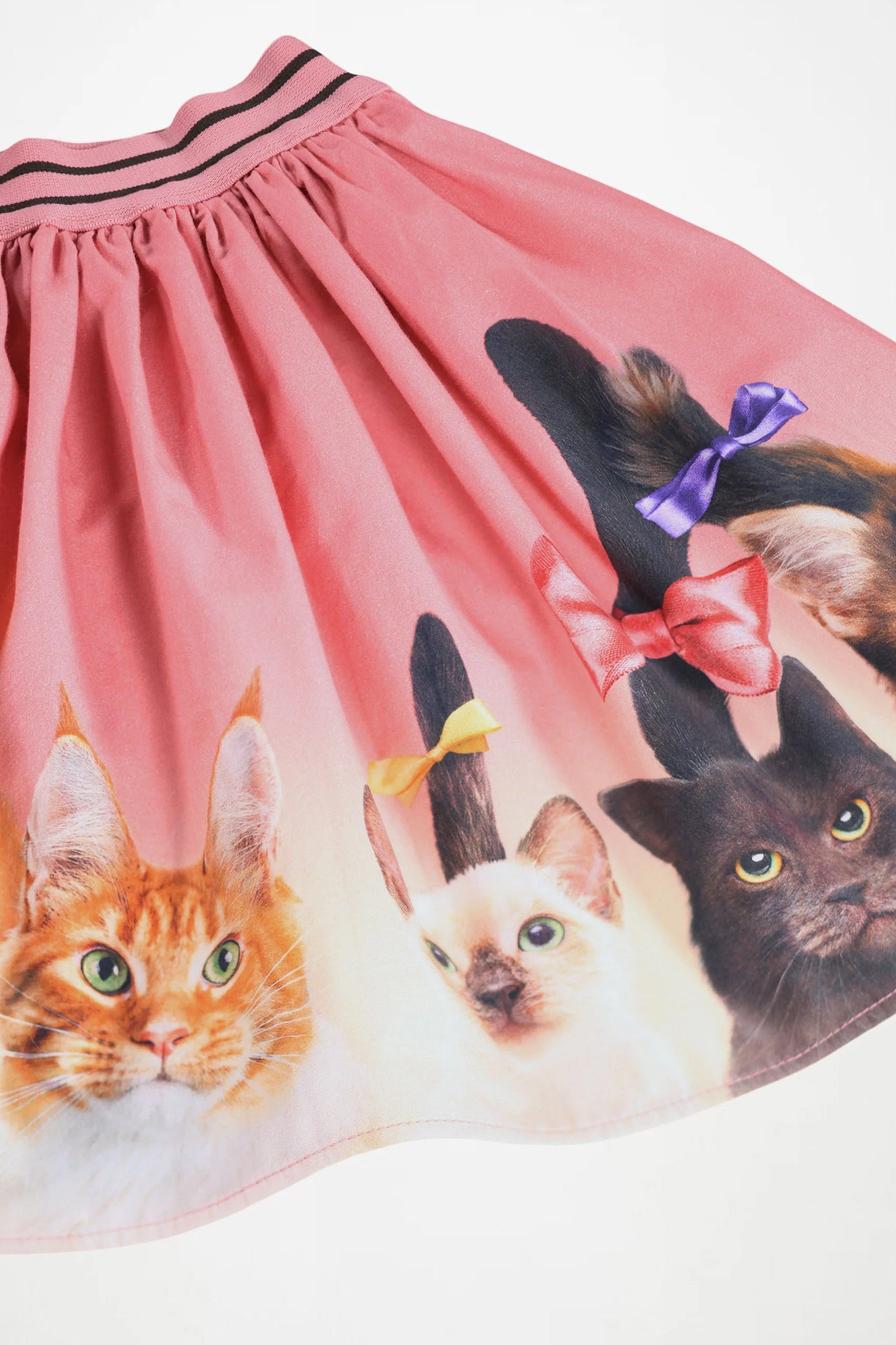 A pink skirt featuring a printed design of three cats with colorful bows on their tails, shown against a plain white background.