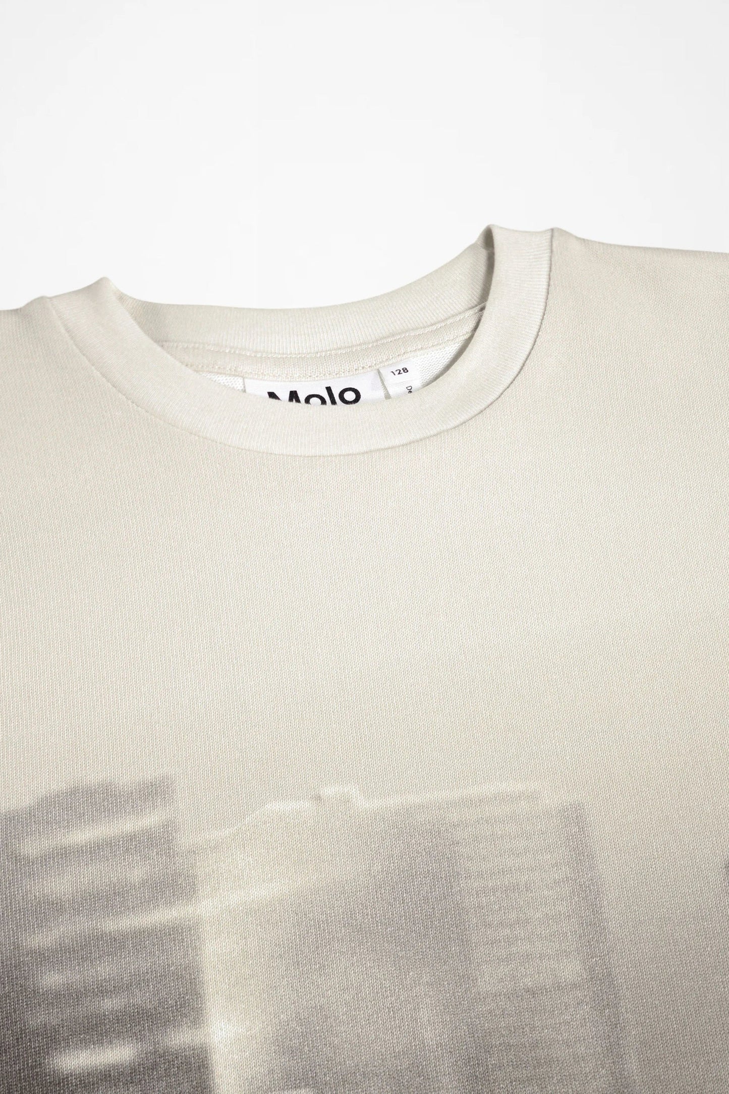 Close-up of a light beige crewneck sweatshirt with a faint, low-contrast graphic print across the lower half and a visible 'Molo' brand tag inside the collar.