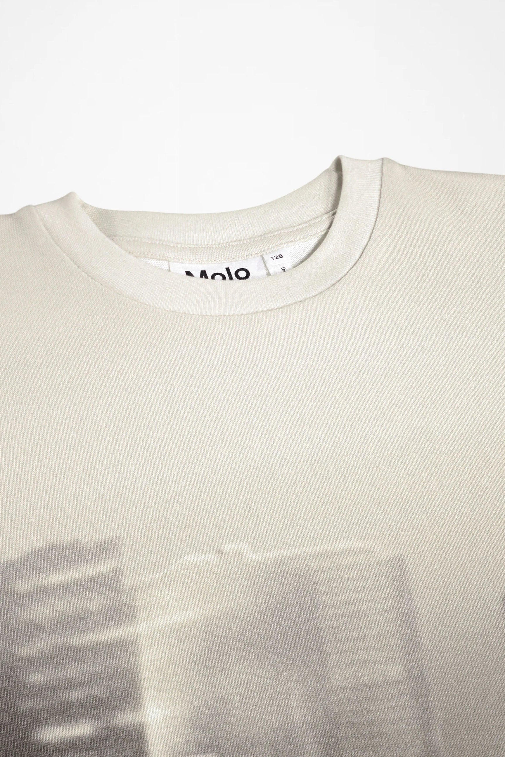 Close-up of a light beige crewneck sweatshirt with a faint, low-contrast graphic print across the lower half and a visible 'Molo' brand tag inside the collar.