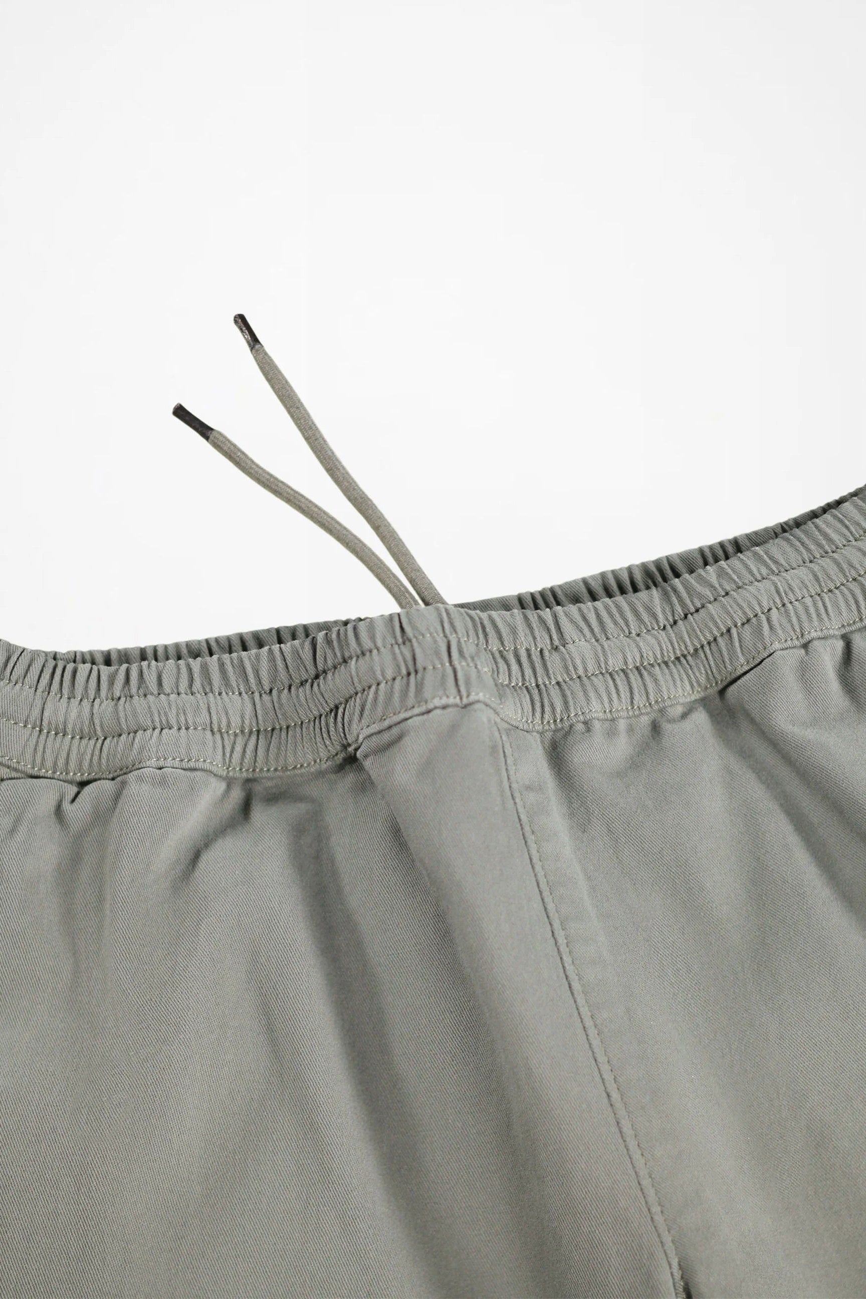 Close-up of a pair of light gray drawstring shorts showing the elastic waistband and drawstrings against a plain white background.