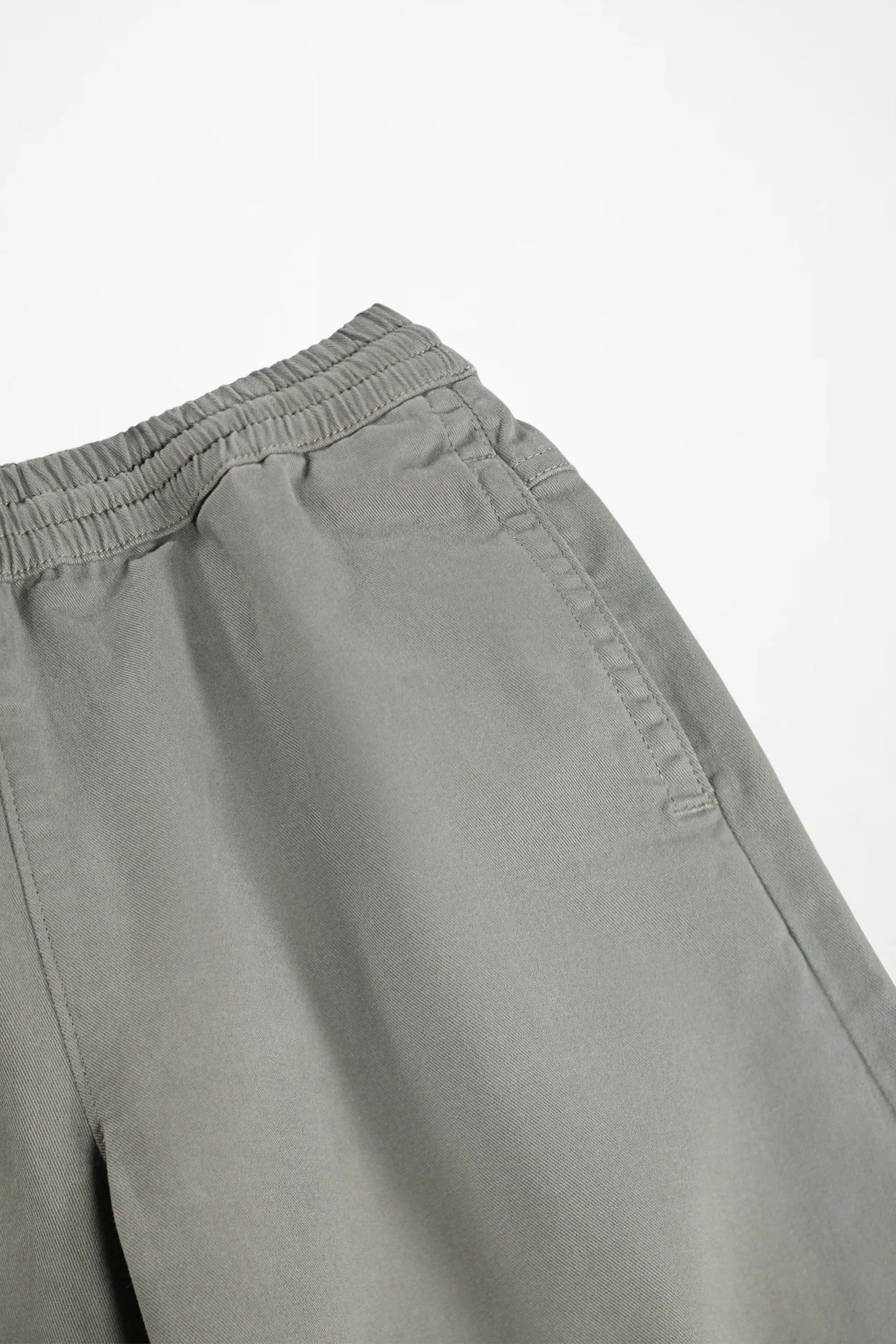 Close-up of a pair of light gray trousers showing the elastic waistband and side pocket detail against a plain white background.