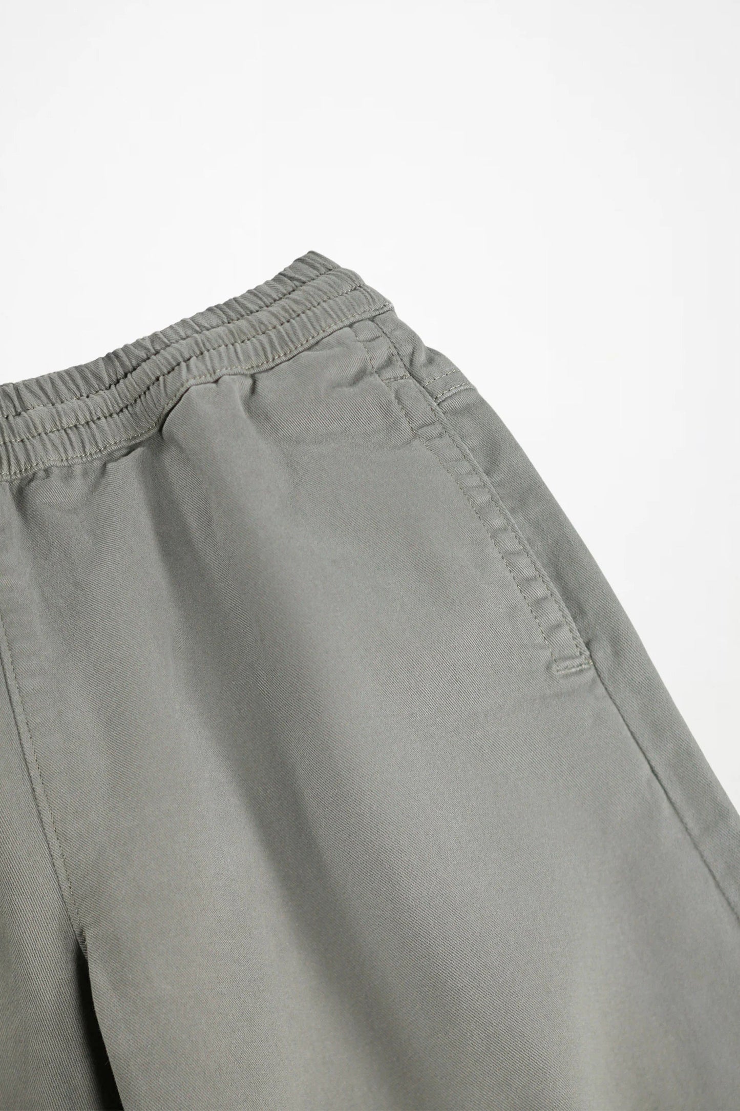 Close-up of a pair of light gray trousers showing the elastic waistband and side pocket detail against a plain white background.