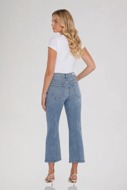 A woman is shown from the back wearing light-wash bleu ciel cropped flare jeans, a white short-sleeve top, and beige high-heeled sandals against a plain light gray studio background.