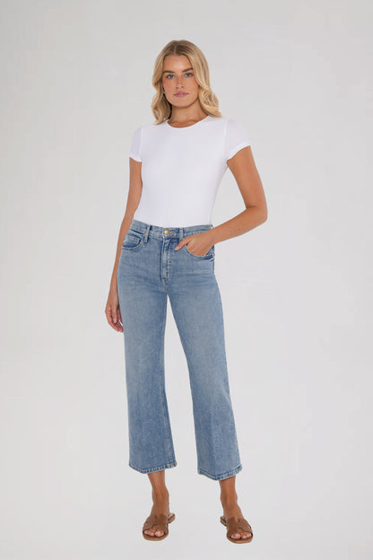 Woman wearing a white t-shirt and bleu ciel jeans on a plain background