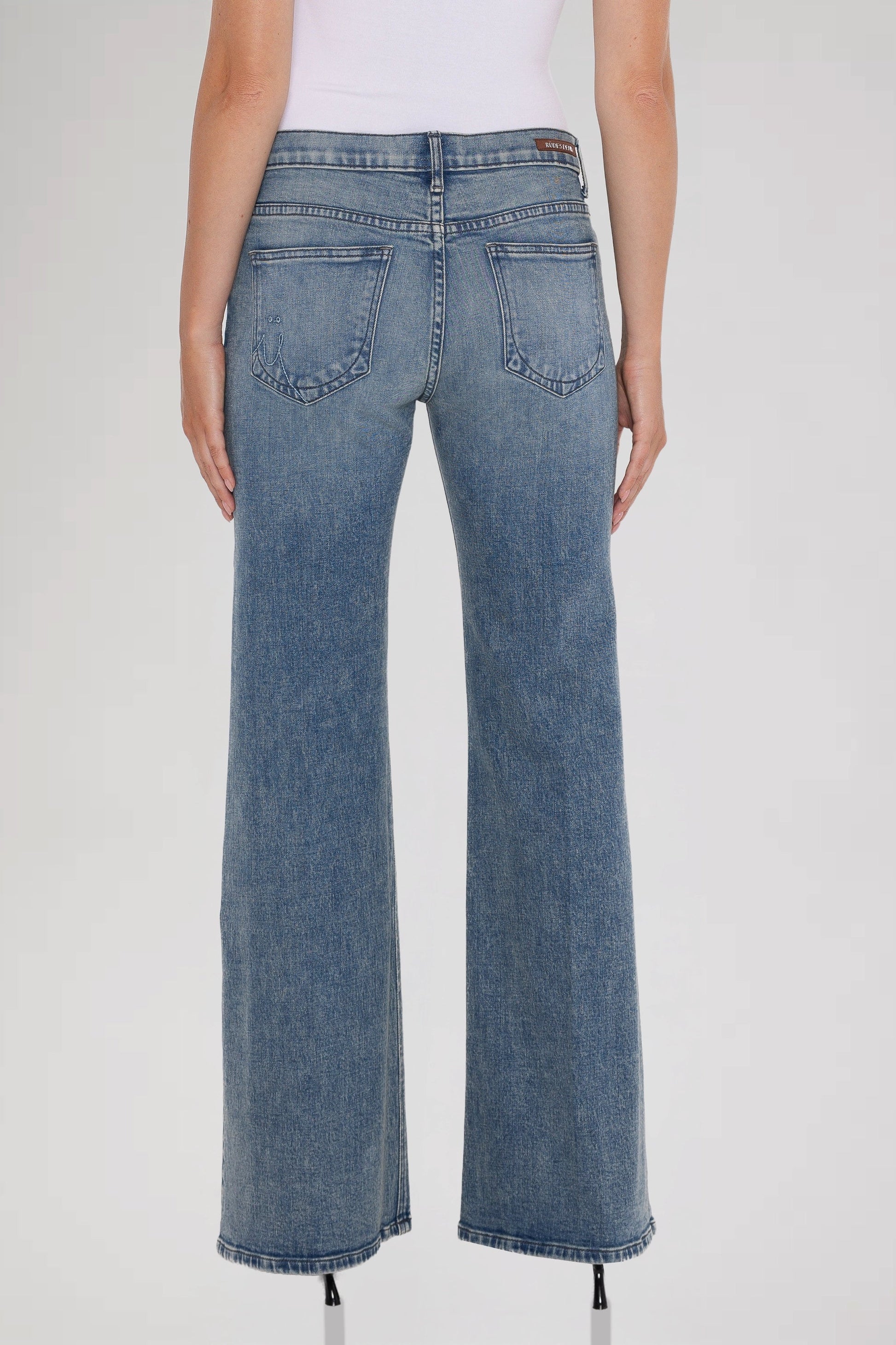 Woman wearing a white sleeveless top and bleu perle grace mid rise jeans standing against a plain background