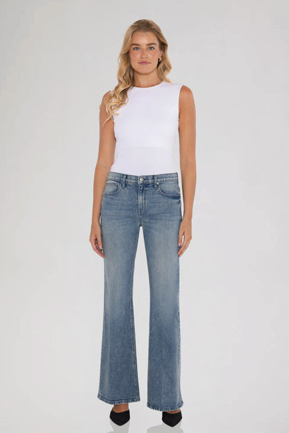 Woman wearing a white sleeveless top and bleu perle grace mid rise jeans standing against a plain background