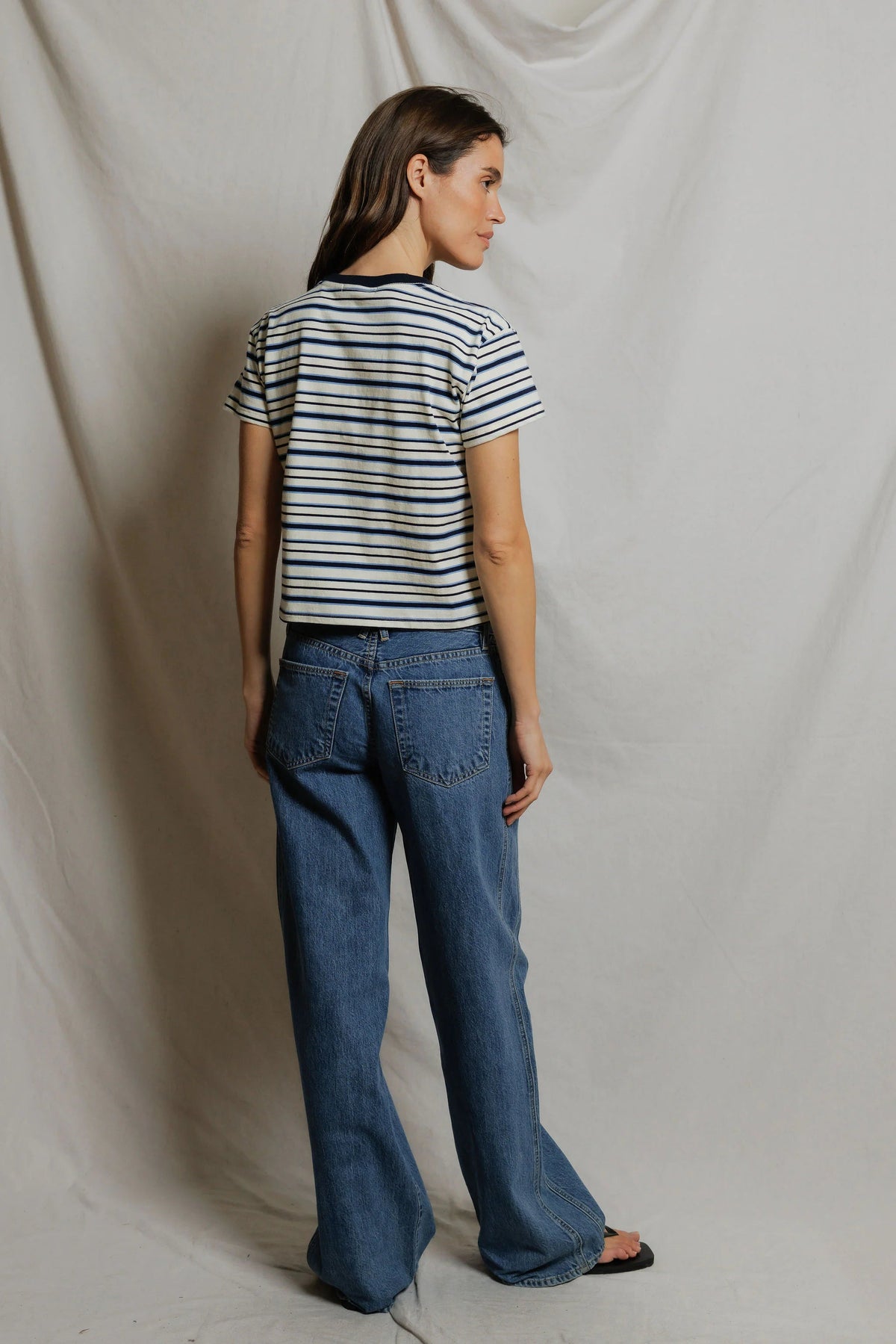 Woman shown from the back wearing a Dawn Jersey Ringer striped shirt in Navy Pacific Stripe and baggy blue jeans against a plain background