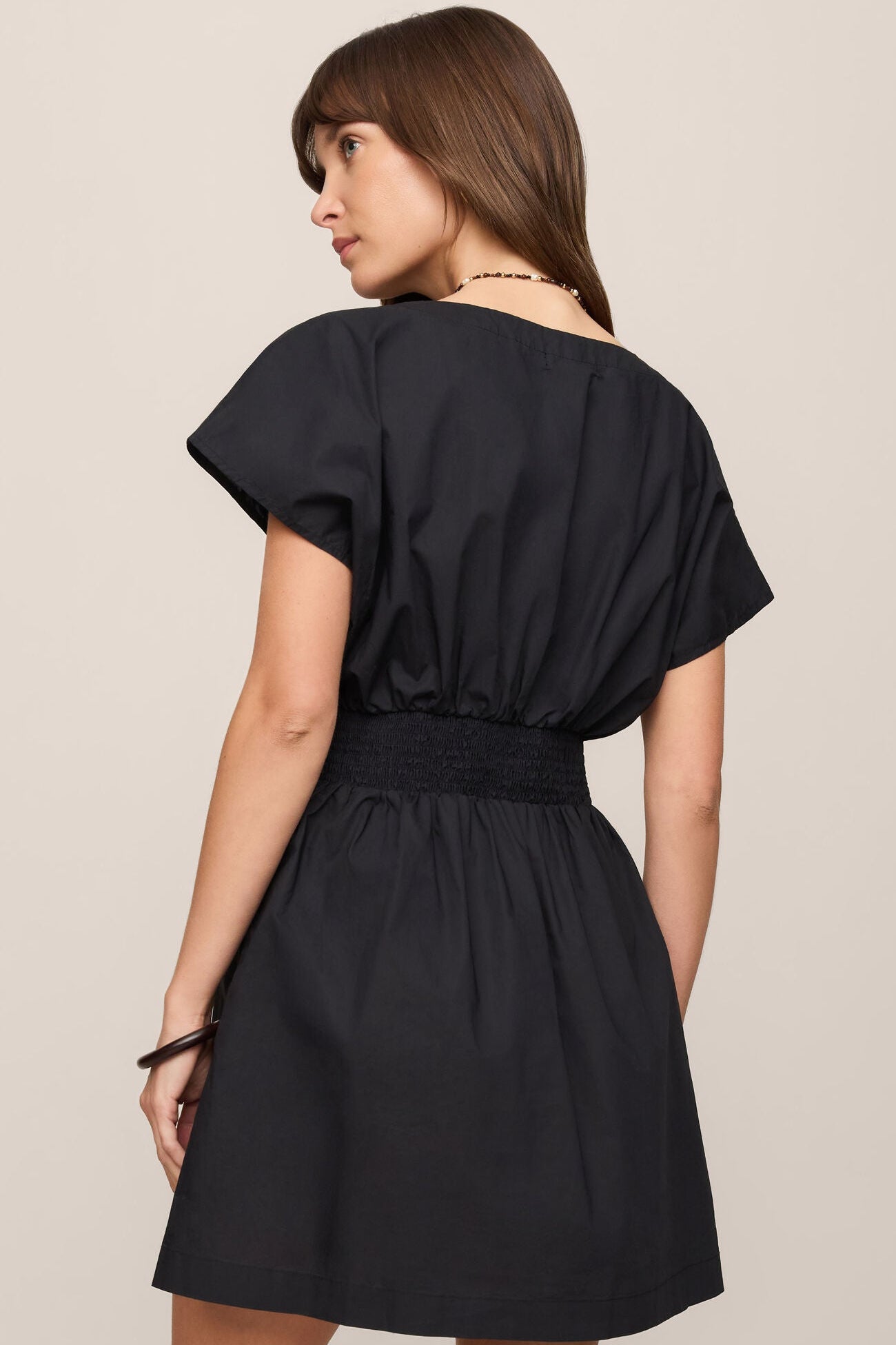Back view of woman wearing the black sanna mini dress against a beige background
