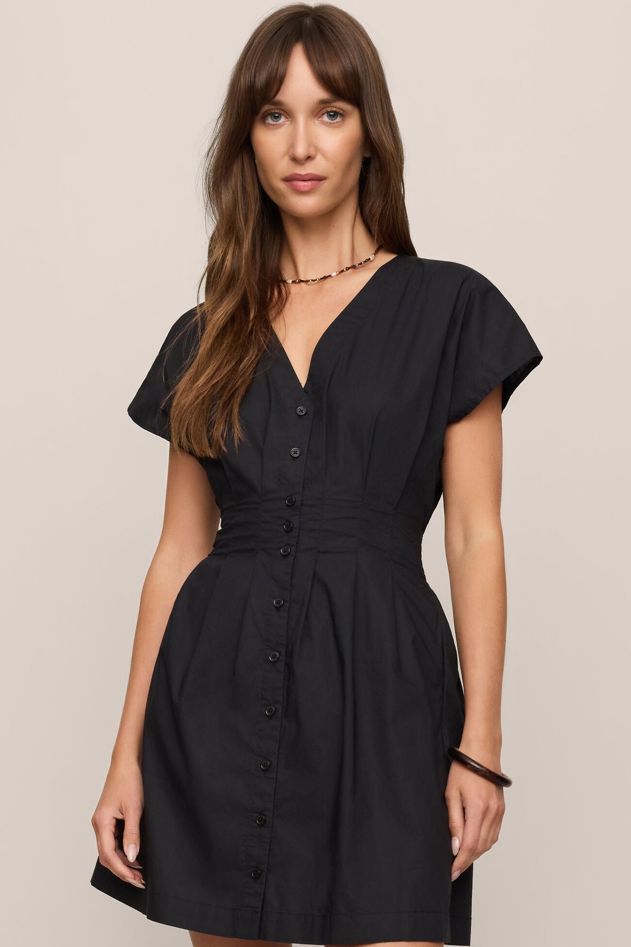 Woman wearing the black sanna mini dress against a beige background