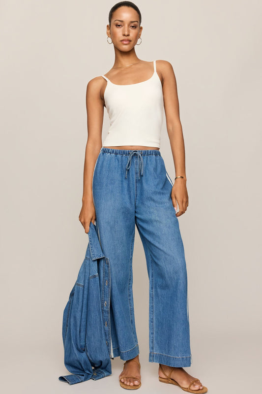 Blue denim track pants with elastic waistband, drawstring, and wide-leg silhouette.