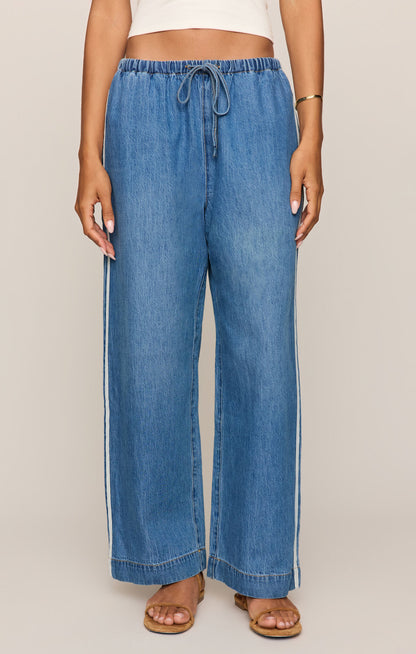 Front view of Woman wearing a white tank top and sidelines denim track pant on a beige background