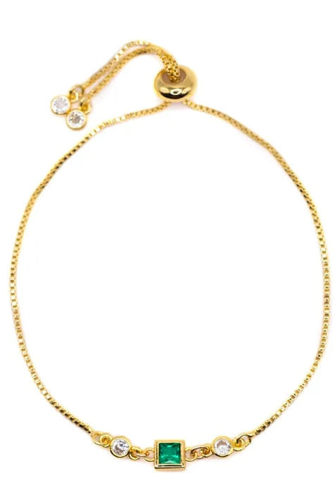 A delicate gold chain bracelet featuring a central square-cut green emerald stone, flanked by two small clear round-cut stones, displayed on a clean white background.