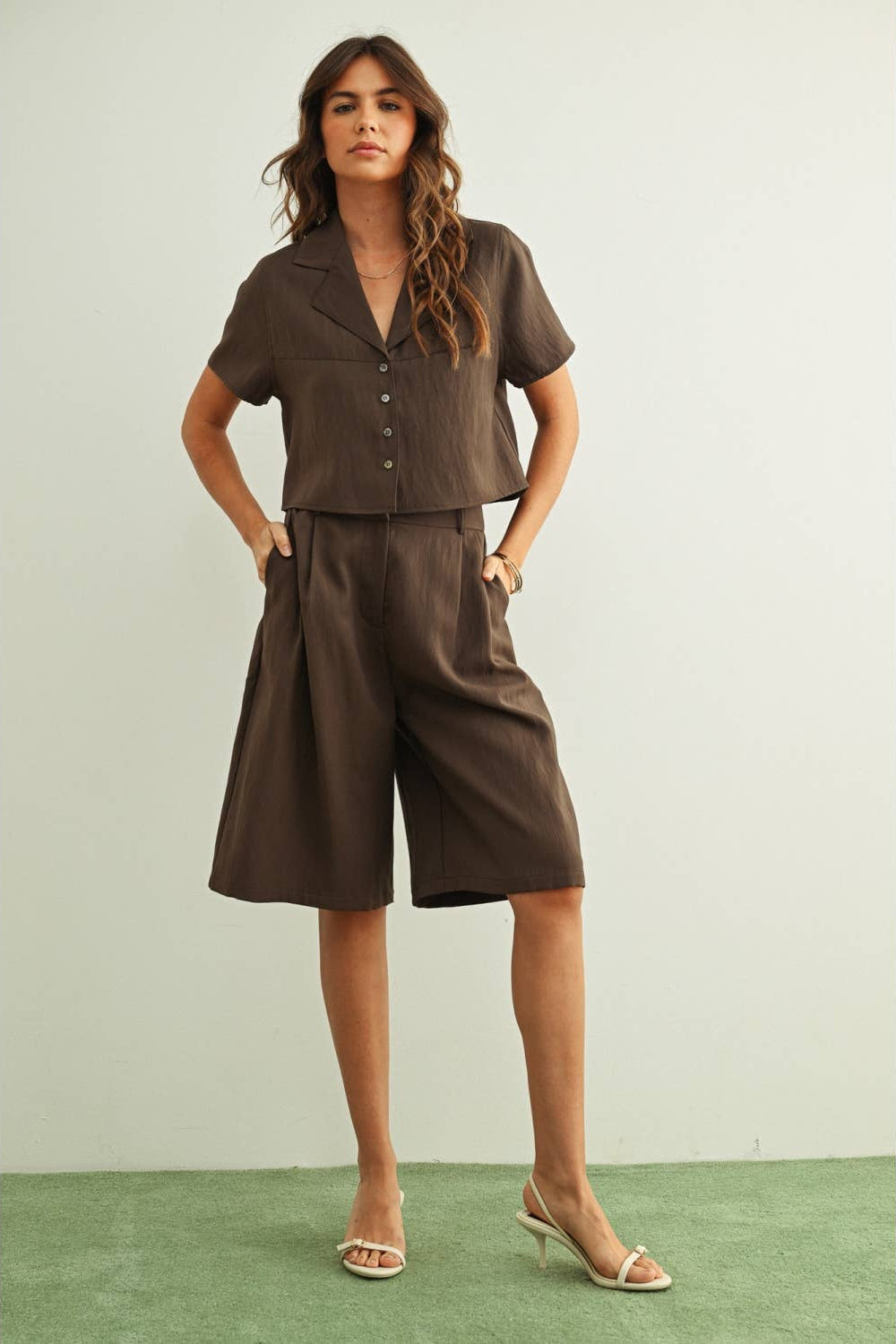 Woman wearing a brown outfit with a top and wide-leg pants against a light green background