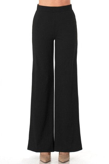 Black wide-leg pants shown on a model from the waist down, paired with beige pointed-toe heels against a plain white background.