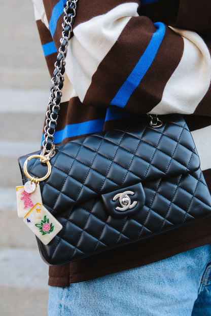 Black quilted handbag with mahjong keychain held by a person wearing a striped sweater.
