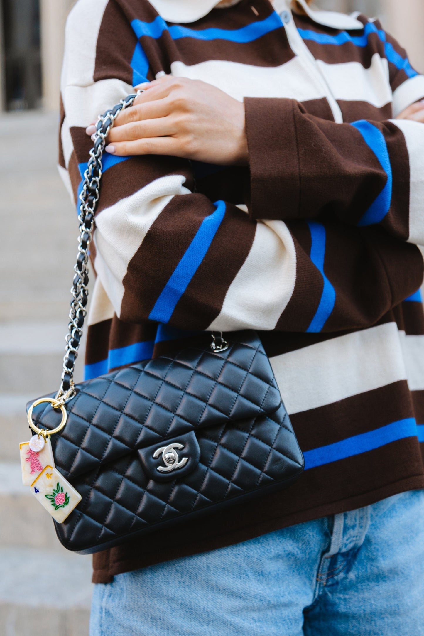 Person holding a black quilted handbag with a mahjong keychain on itwearing a striped sweater and jeans.