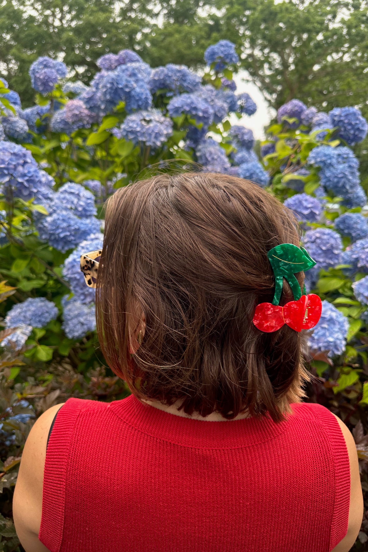 Person with a cherry hair clip in front of blue hydrangeas