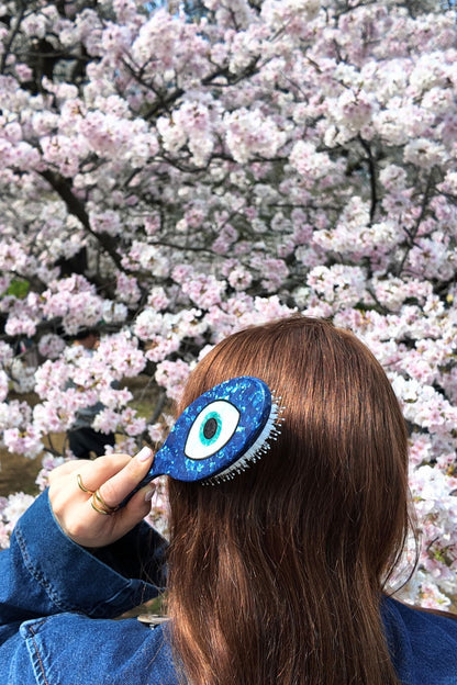 Person using a hairbrush with an evil eye design against a cherry blossom background