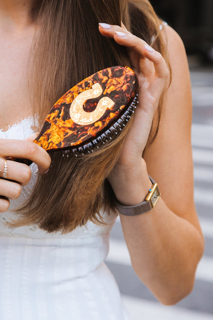 Person using a tortoiseshell hairbrush with a gold horseshoe design 