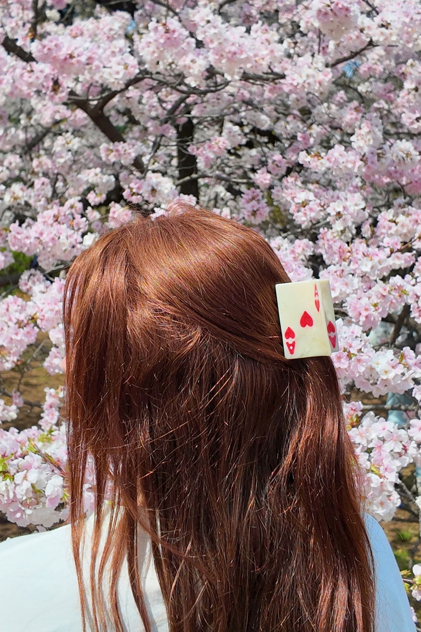 Person with a hair clip featuring ace of hearts against a cherry blossom background
